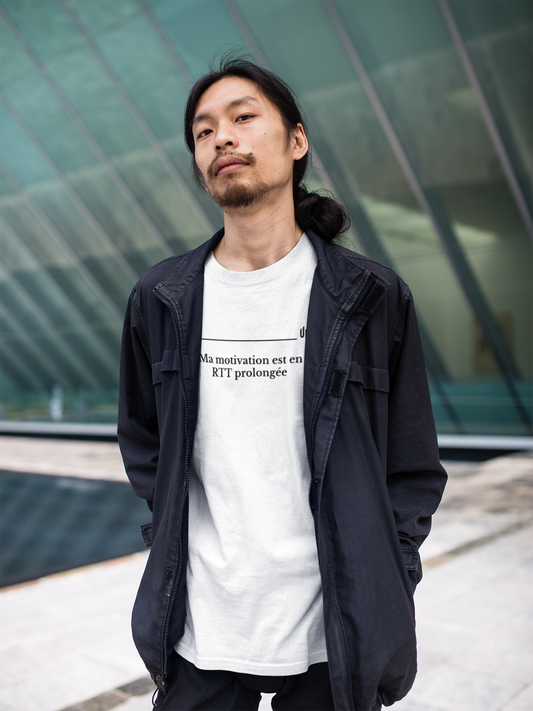 Man wearing a black jacket and white t-shirt with text, standing in front of a modern building.
