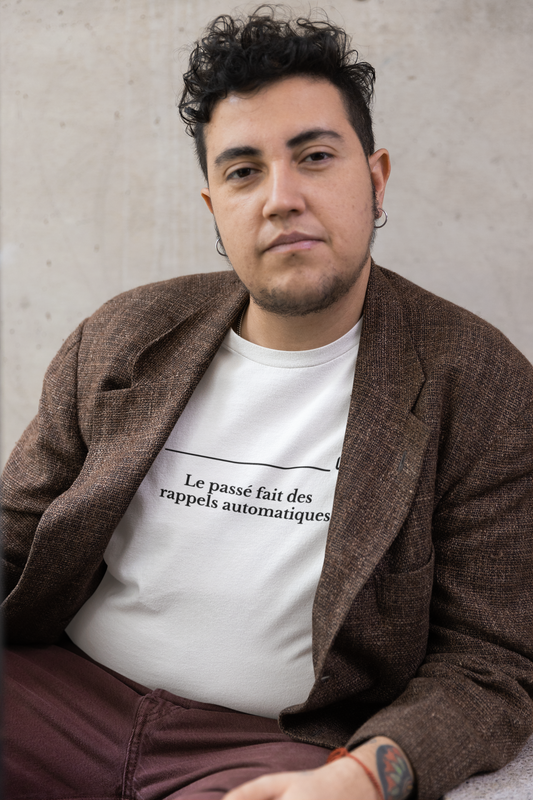 Man wearing a brown blazer over a white shirt with text, sitting against a plain background