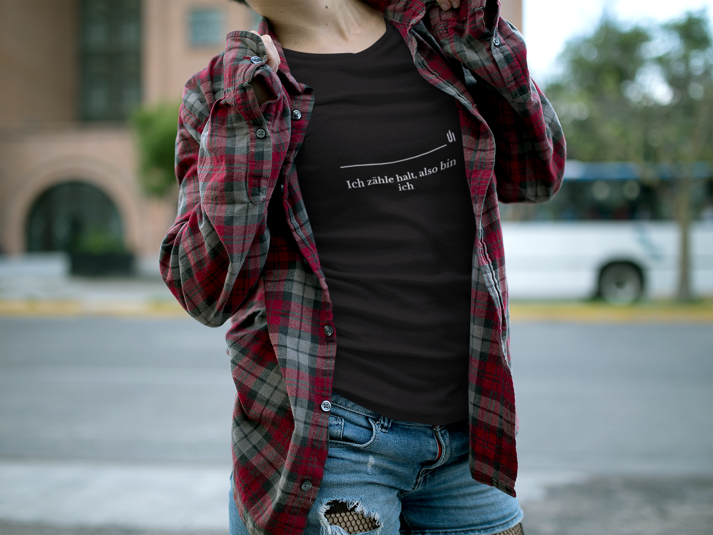 Person wearing a black t-shirt with text and a red plaid shirt over shoulders outdoors.