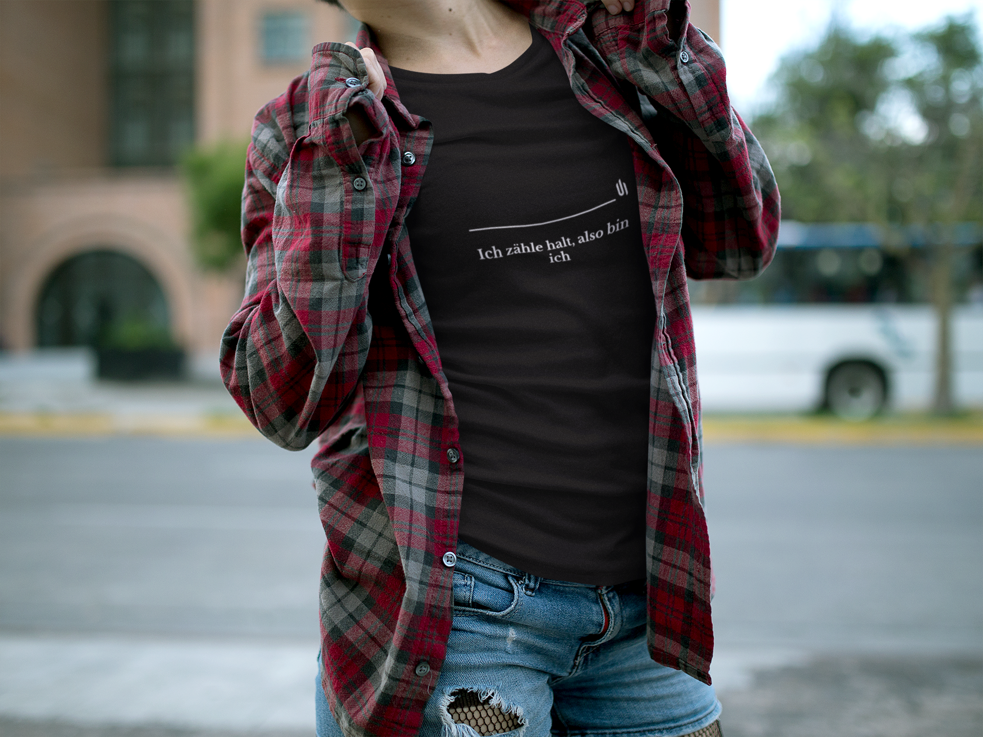 Person wearing a black t-shirt with text and a red plaid shirt over shoulders outdoors.