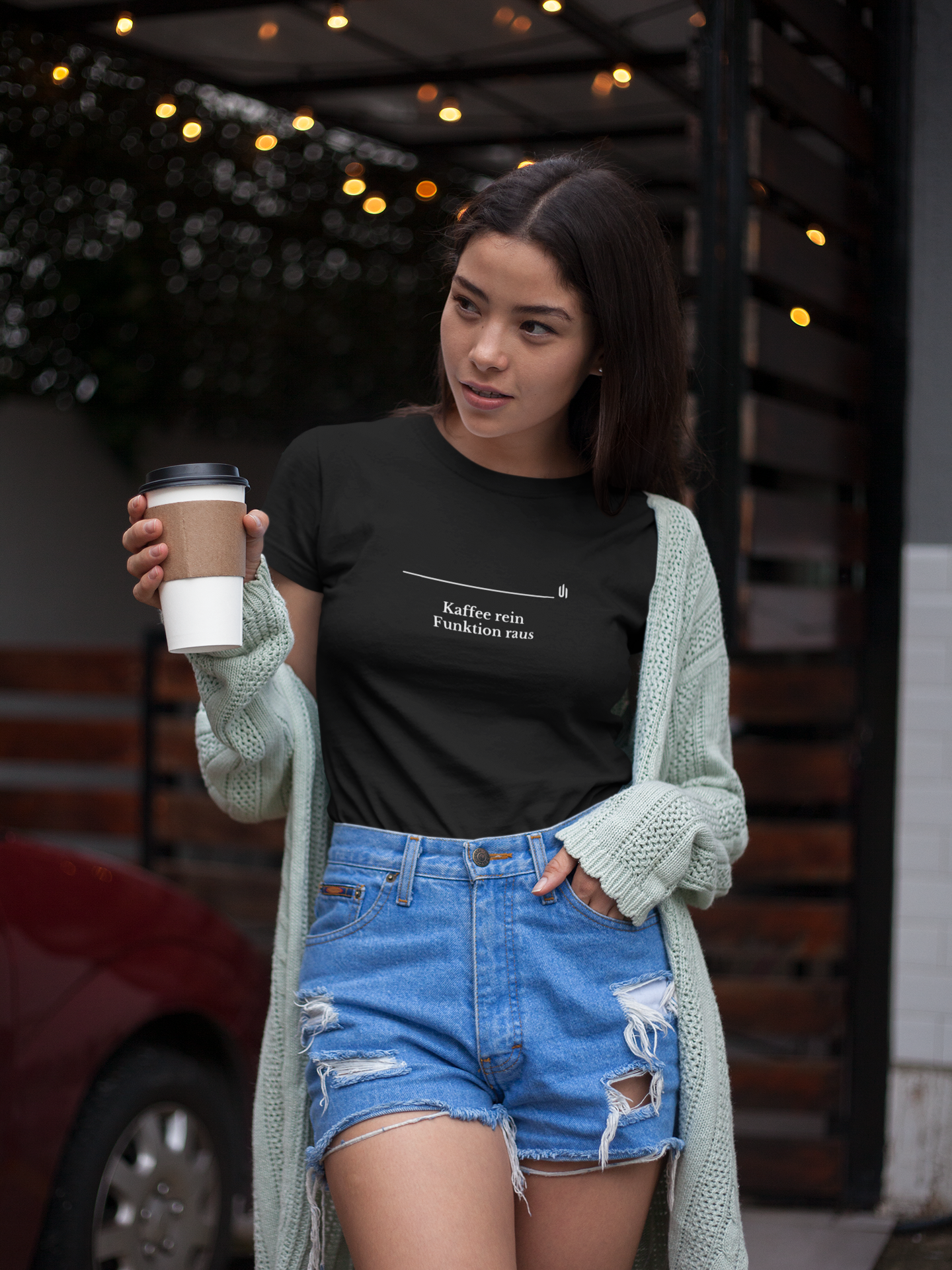 Woman holding a coffee cup wearing a black t-shirt and denim shorts outdoors.